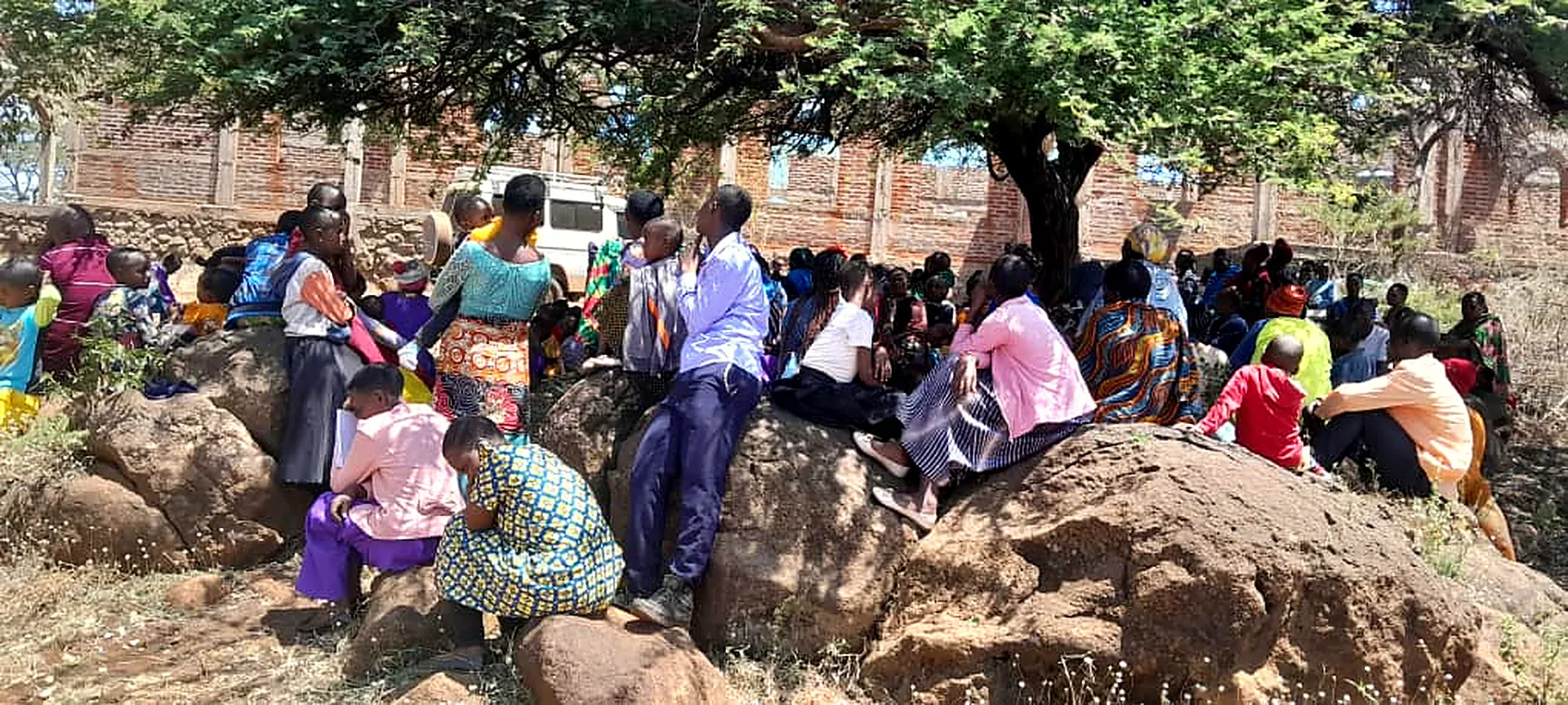 The congregation seated on the rocks under an acacia, against the wall of the unfinished church.